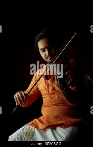 A serene musician in traditional Indian clothing plays the violin against a dark background. The image captures concentration and passion, highlightin Stock Photo