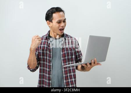 Happy asian indonesian man holding laptop computer on isolated background Stock Photo