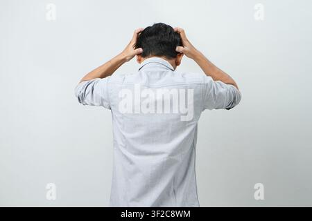 back view of asian indonesian man with hand grab his head showing stressful confused gesture. isolated background Stock Photo