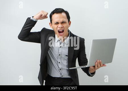 Angry mad asian indonesian business man in suit holding laptop computer on isolated background Stock Photo