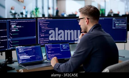 Young Software Engineer Coding Secure Algorithms On Laptop At Busy Office Desk. Stock Photo