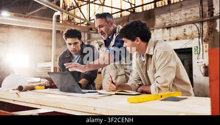 Carpenter, team and laptop in warehouse for planning, project management and help for apprentice. Men, tech and discussion in woodworking factory for Stock Photo