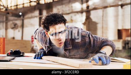 Carpenter, sanding and man blow dust in workshop with wood for clean, productivity or production. Person, safety gear and warehouse with tools for Stock Photo