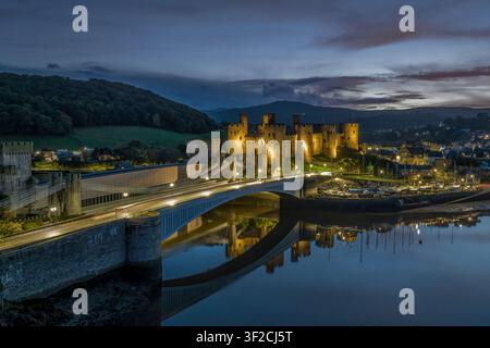Conwy Castle at dusk, Conwy, North Wales. Aerial view over the harbour with Snowdonia mountains beyond the medieval fortress. Stock Photo