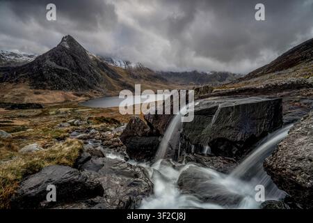 Snowdonia, Wales – waterfall in the Ogwen Valley with the dramatic mountain peak of Tryfan rising above the rugged landscape. Stock Photo
