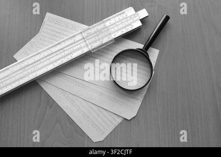 Retro calculation tools and vintage punched cards with a magnifying glass on a wooden surface, monochrome math and engineering flat lay concept Stock Photo