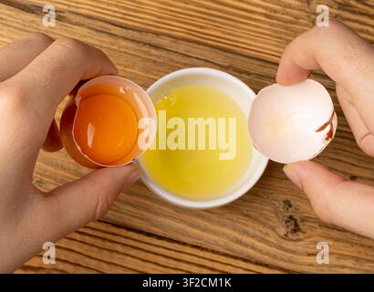 Broken Egg in Hand, Raw Yolk and White Separation, Cracked Brown Shell, Fresh Broken Organic Chicken Eggs on Wooden Rustic Background Stock Photo