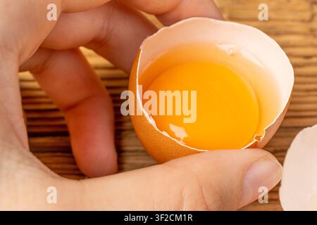 Broken Egg in Hand, Raw Yolk and White Separation, Cracked Brown Shell, Fresh Broken Organic Chicken Eggs on Wooden Rustic Background Stock Photo