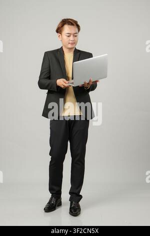 full lenght shoot of happy cheerful asian business man wearing suit holding laptop computer on isolated background Stock Photo