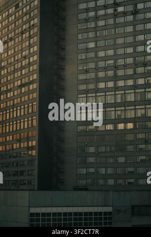 Monumental modernist concrete high-rise facade featuring repeating window grids reflecting warm golden hour sunset light. Stock Photo