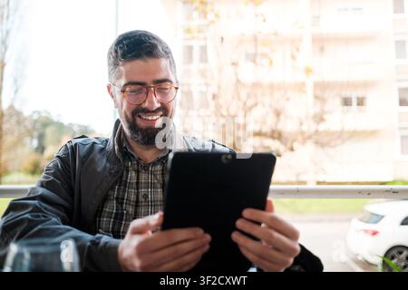 Bearded man smiling outdoors while using a digital tablet for communication and entertainment Stock Photo