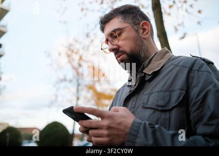 Man wearing glasses and jacket browsing content or typing on his mobile phone Stock Photo
