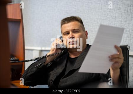 Businessman working with documents while talking on the phone in the office. Corporate negotiations, business communication, paperwork review and prof Stock Photo