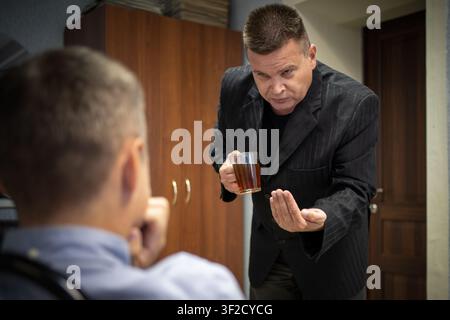 Serious businessman holding a glass mug of tea and gesturing with his hand, explaining something to colleague. Office negotiation, professional disagr Stock Photo