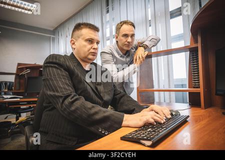 Two male office workers looking at a computer screen together, one typing on the keyboard. Teamwork, professional collaboration, and workplace problem Stock Photo