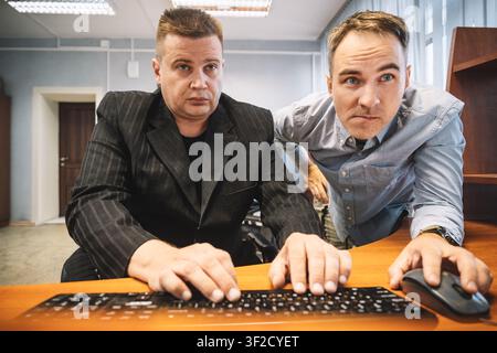 Two male office workers looking at a computer screen together, one typing on the keyboard. Teamwork, professional collaboration, and workplace problem Stock Photo