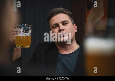 Friends enjoying beer at a bar, one raising toast. Cheerful drinking moment. Stock Photo
