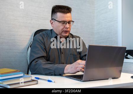 Tired businessman yawning while working on a laptop in the office, struggling with fatigue, overtime, burnout, and lack of sleep during a busy workday Stock Photo