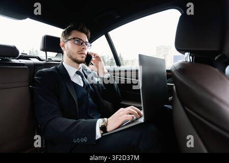 Young businessman talking on phone in car using his pc Stock Photo