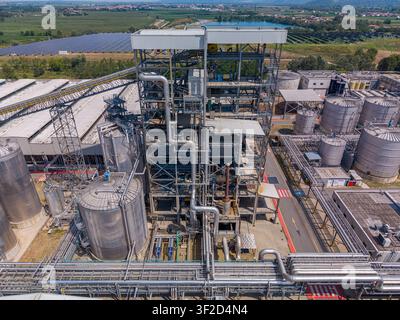 Aerial view of an industrial facility featuring complex metal structures, storage tanks, and extensive piping systems surrounded by solar panels in Cr Stock Photo