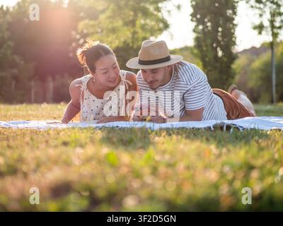 Multiracial couple spending time in park in summertime. They are using smartphone. Stock Photo