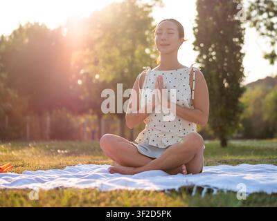 Adult woman is practicing yoga in park in summertime. Lotus position. Stock Photo