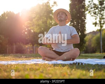 Adult man is practicing yoga in park in summertime. Lotus position. Stock Photo