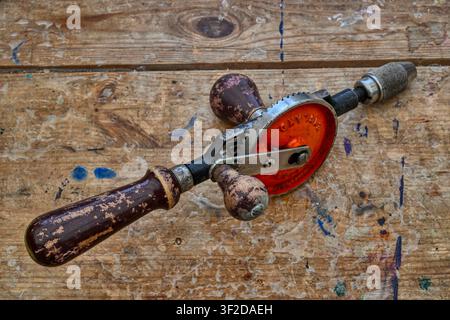 Old hand drill on a weathered wooden workbench top Stock Photo