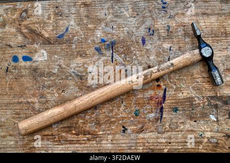 Old hammer on a stained and weathered work bench top Stock Photo