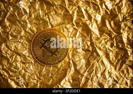 Physical Bitcoin token centered on crumpled metallic gold foil, symbolizing cryptocurrency, wealth and digital finance Stock Photo