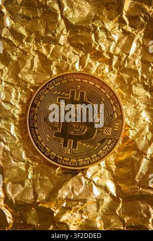 Physical Bitcoin token centered on crumpled metallic gold foil, symbolizing cryptocurrency, wealth and digital finance Stock Photo