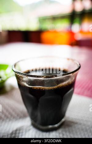 Glass cup of fresh black coffee sitting on a red checkered tablecloth at an outdoor cafe table Stock Photo