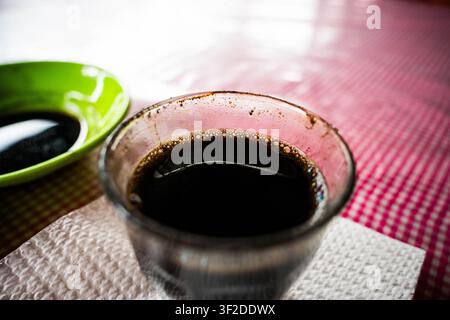 Glass cup of fresh black coffee sitting on a red checkered tablecloth at an outdoor cafe table Stock Photo