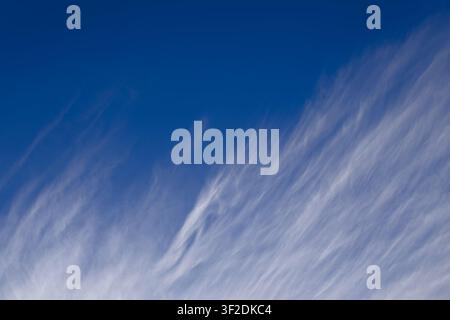 Wispy white cirrus fibratus clouds streak across a vivid deep blue sky in the high-altitude upper atmosphere. Stock Photo