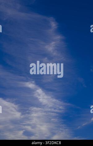 Soft cirrus fibratus clouds cascade vertically across a deep blue sky like abstract ocean waves in the upper atmosphere. Stock Photo