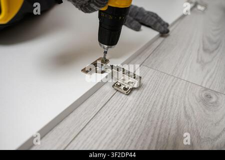 Furniture assembly. Close-up of man installing hidden cabinet hinge using screwdriver. Concept: interior design, real estate development, flat pack fu Stock Photo
