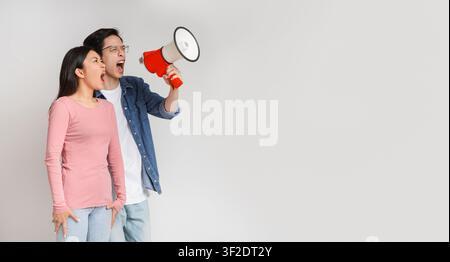 Angry asian couple shouting together through megaphone Stock Photo