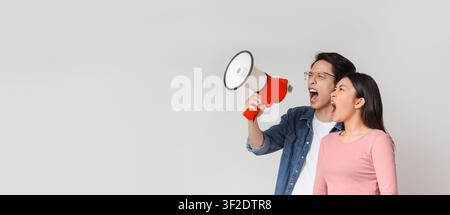 Emotional young asian couple with megaphone screaming towards copy space Stock Photo