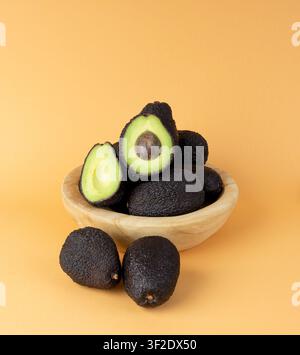 Whole Avocado Hass in Bowl, Whole Sharwil, Brown Avocados Cut, Fresh Alligator Pear, Guacamole Ingredient, Persea Americana Avocado Fruit on Orange Ba Stock Photo