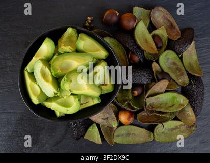 Many Hass Avocado Slices and Peel on Black Background, Brown Avocados Cuts Pattern, Fresh Alligator Pear Pieces, Compost Ingredient, Persea Americana Stock Photo