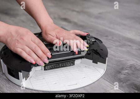Close up of woman hands opening main brush cover of robot vacuum cleaner. Stock Photo