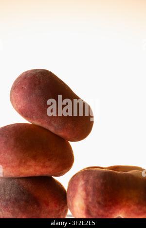 Dark smooth peaches stacked in a tower against a warm glowing background. Minimal zen still life composition, earthy tones, balance and calm concept. Stock Photo