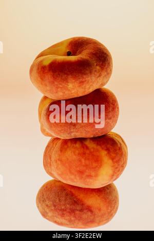 Three flat peaches stacked vertically in a tower on a warm gradient background. Clean studio still life with copy space, vertical composition. Stock Photo