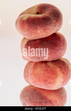 Stack of flat peaches on white background with soft reflection below. Clean minimal studio still life, reflective surface, summer fruit composition. Stock Photo