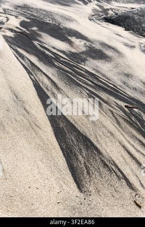 Dark patches forming natural designs in the light beach sand, flanked by scattered stones, creating an abstract visual. Stock Photo