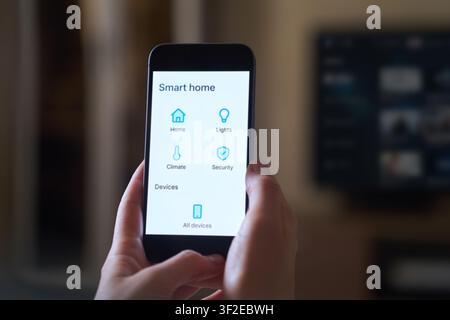 Person holding a smartphone displaying a smart home app interface. The screen shows options for controlling home, climate, lights, and security device Stock Photo