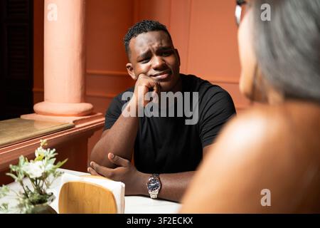 Multicultural Venezuelan and Dominican couple in an outdoor cafe, having a serious conversation. Man listens thoughtfully to partner across the table Stock Photo