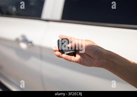 Close-up of a person holding a car key fob and pressing the unlock button near a white vehicle door, highlighting modern access, security, and conveni Stock Photo