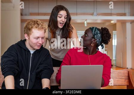 Multiethnic college students collaborate around a laptop in a classroom, discussing ideas and working on a group assignment with teamwork and peer lea Stock Photo