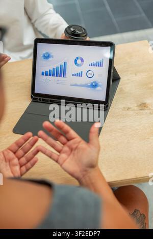 Colleagues discuss performance data at a table while a tablet displays an AI analytics dashboard with charts, graphs, and KPI trends for business plan Stock Photo